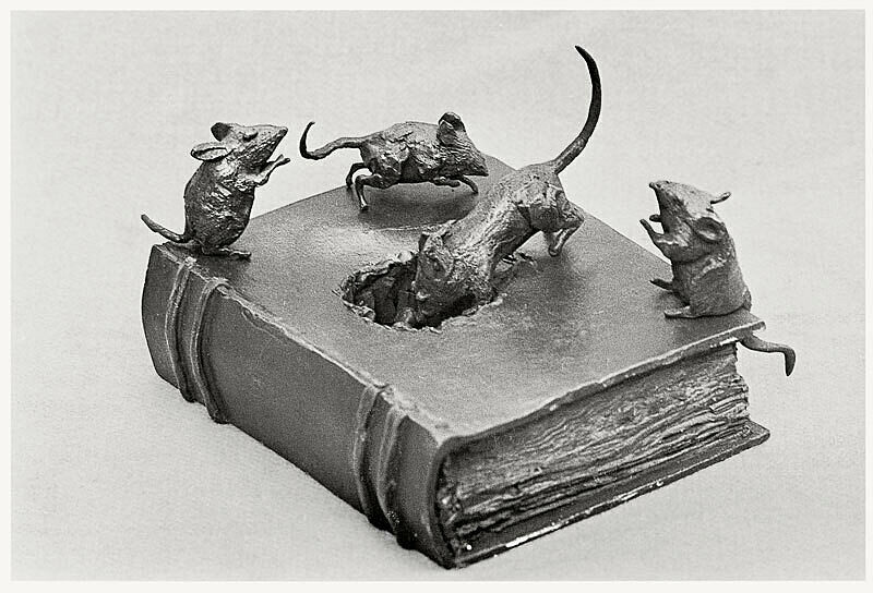 A bronze sculpture of four mice on top of a book, with one of the mice eating a hole through the cover of the book.