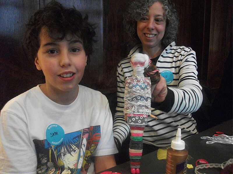 A child and parent show their mummified Barbie to the camera.