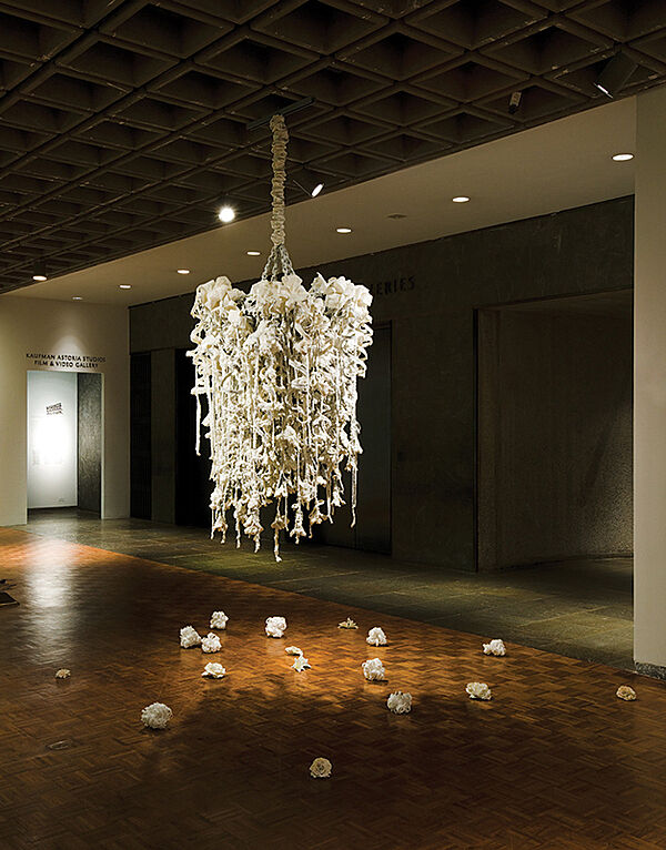 A white sculpture hangs from the ceiling in a gallery.