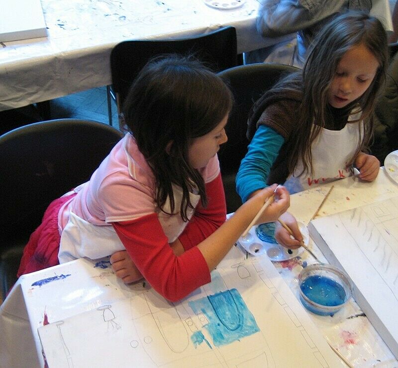 Two children dip their brushes in blue paint