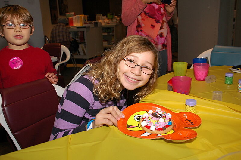 A girl smiles and displays her artwork in the form of a cookie.