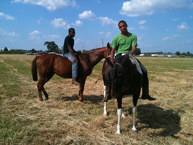 Two men sit on horseback in an open field. 