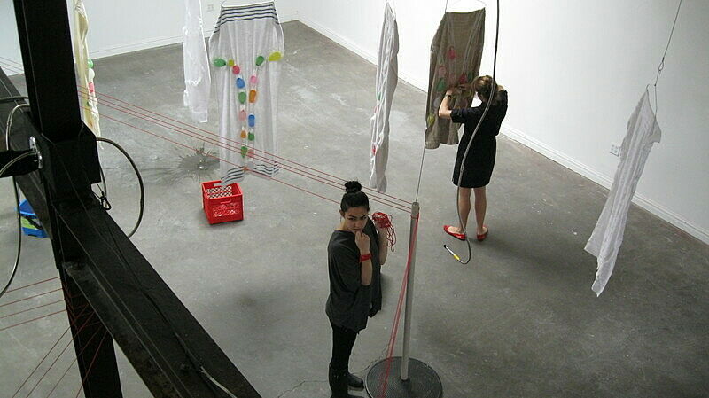 Two people work with string and clothing in the space.
