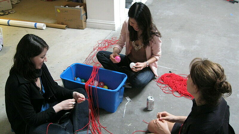Three staff members work with a box of chords and balloons.