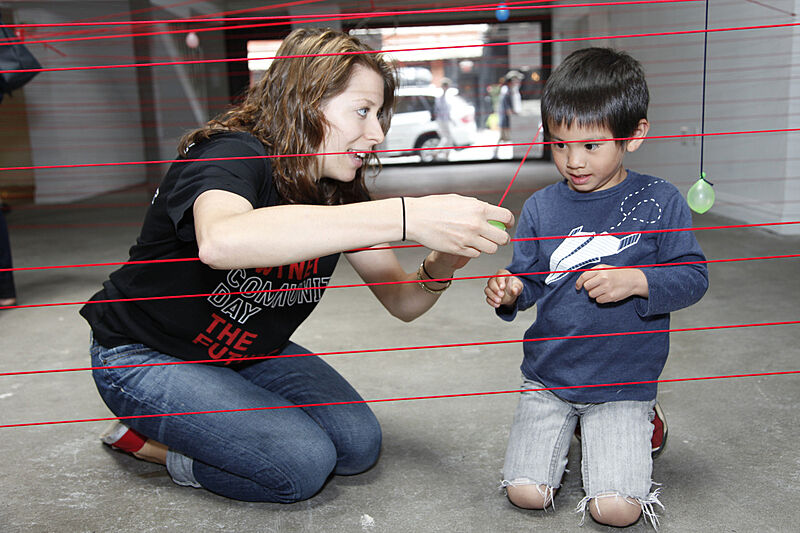 A teacher shows a child how to add more red chords to the installation.