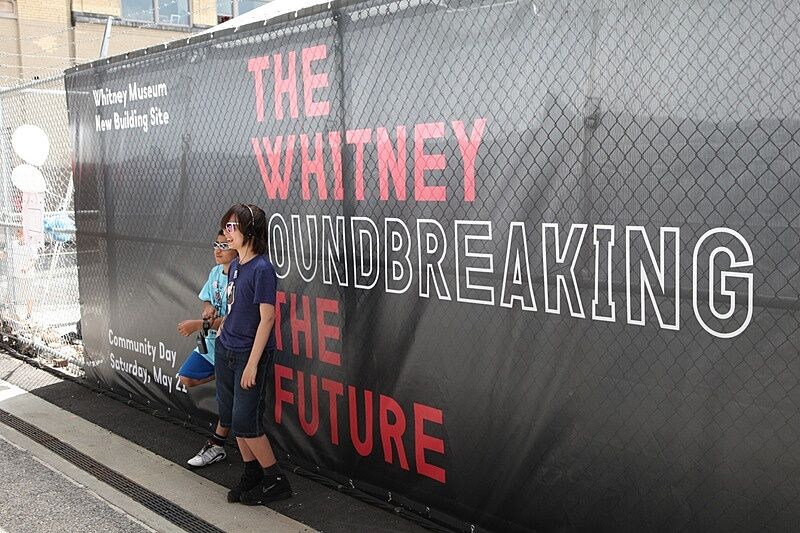 Two kids pose in front of a banner promoting the new Whitney building.
