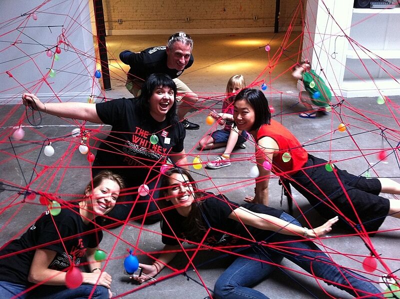 People pose underneath red elastic chords in an art installation.