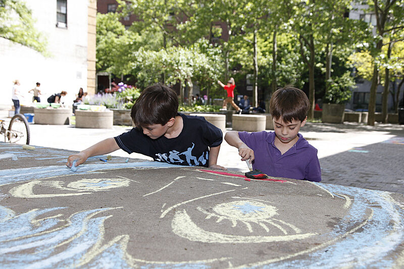 Children work with chalk to make a giant face in an outdoor courtyard.