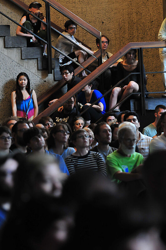 The audience overflows onto the stairs from the gallery. 