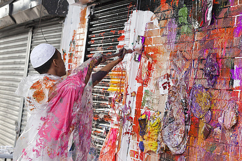 A student uses a mop as a paint brush as he works on a mural.