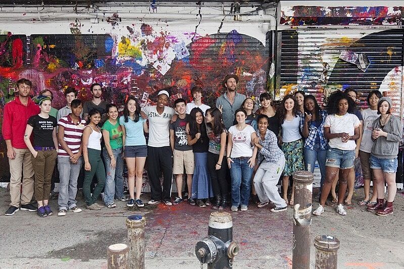 The artist poses with a group of teens in front of the final mural project.