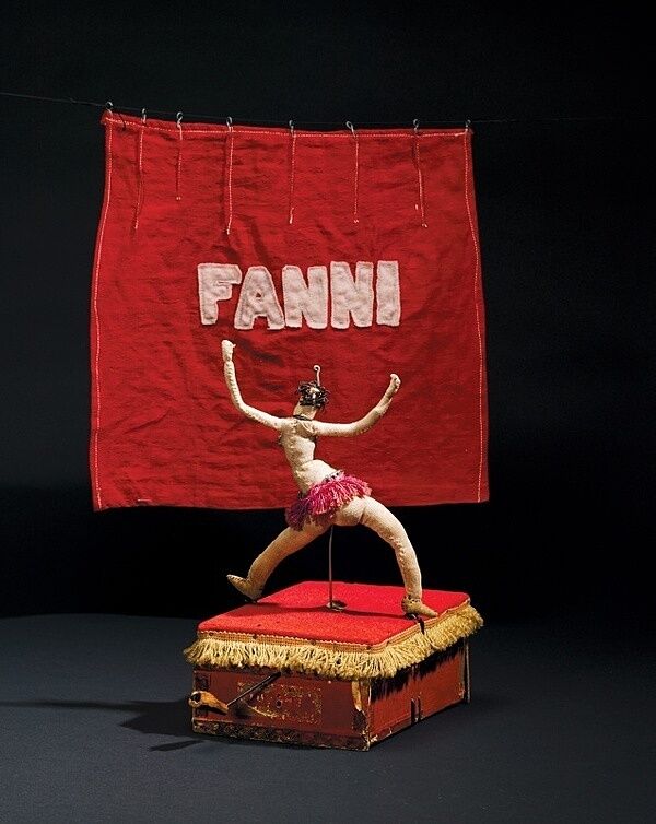 A cloth sculpture of a belly dancer on a red podium.