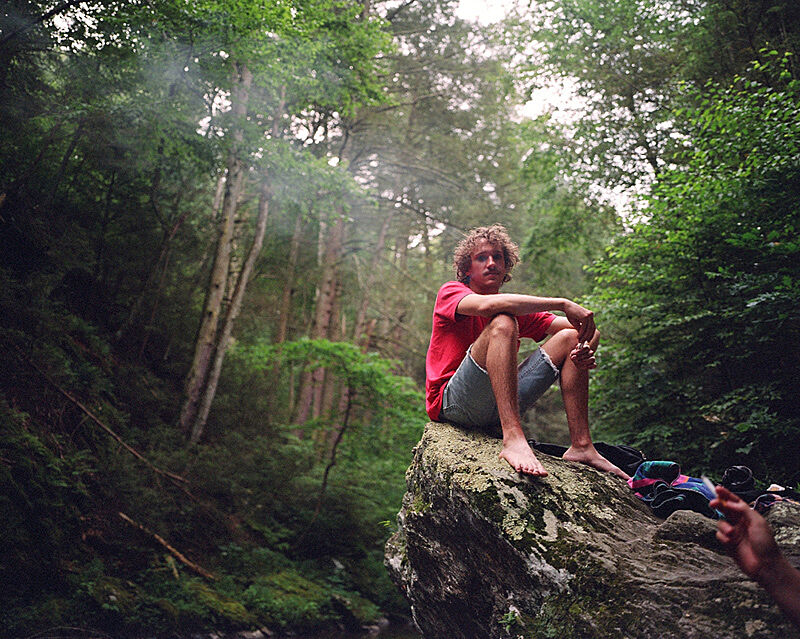 A photograph of a person sitting on a rock in a forrest.