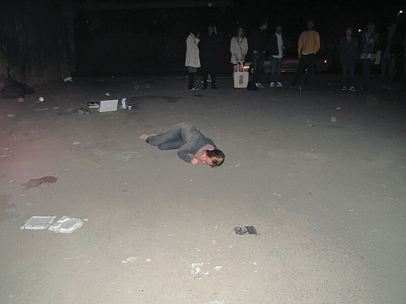 A photograph of a person laying on the dirt ground surrounded by an audience.