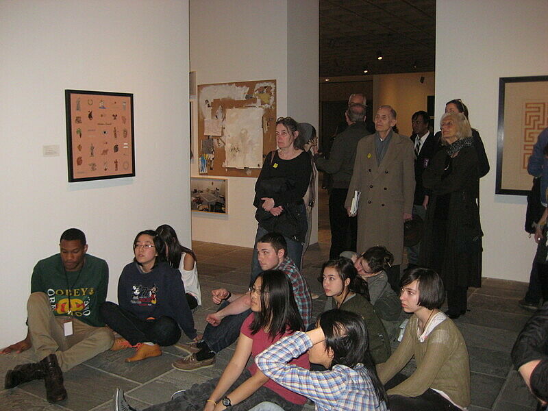 Students sit on the gallery floor while museum guests stand in the back.