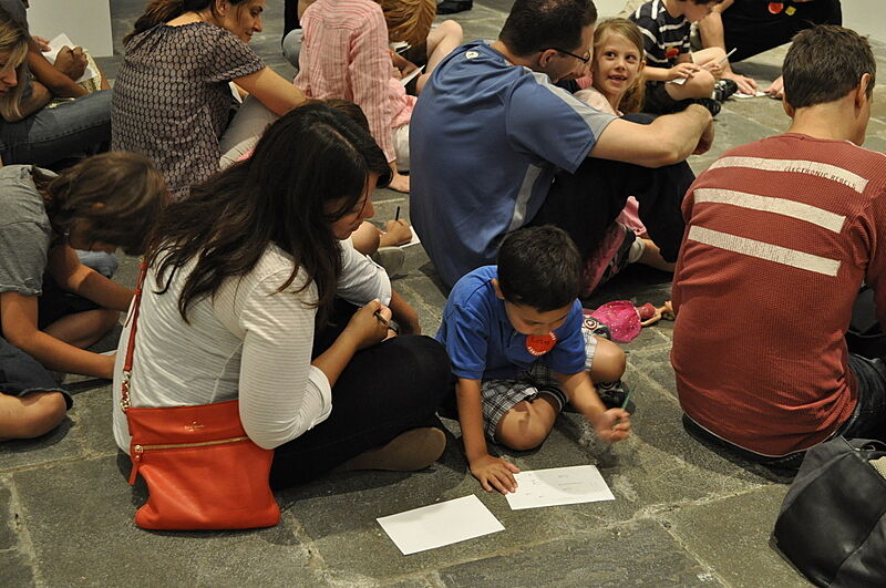 A family sits on the gallery floor and sketches on paper.
