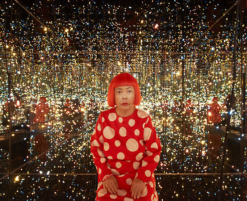 Yayoi Kusama staring at camera in the middle of her mirrored rooms.