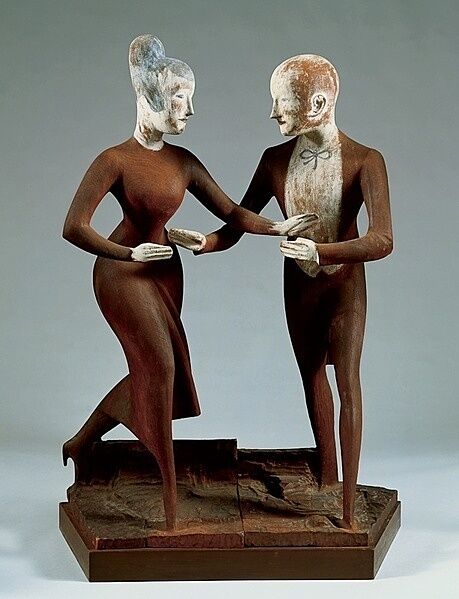 Two elongated figures in brown attire, one male and one female, stand on a textured base, facing each other and holding hands.