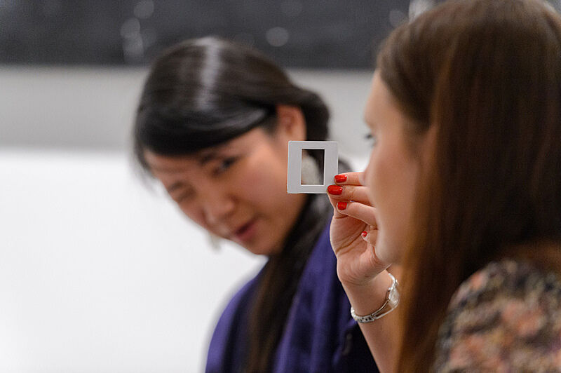 Two women examining a small slide, one holding it up and the other squinting to see it clearly.