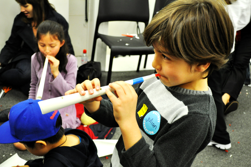 A young boy blows into a home-made instrument.