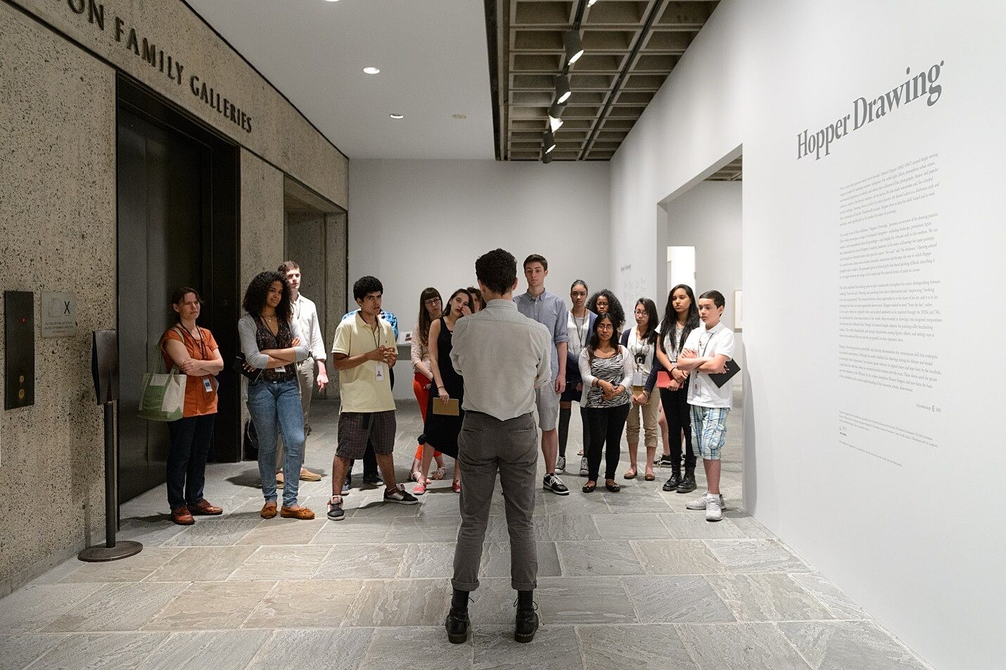 A group of teens stand outside of the Hopper exhibit with a curator.