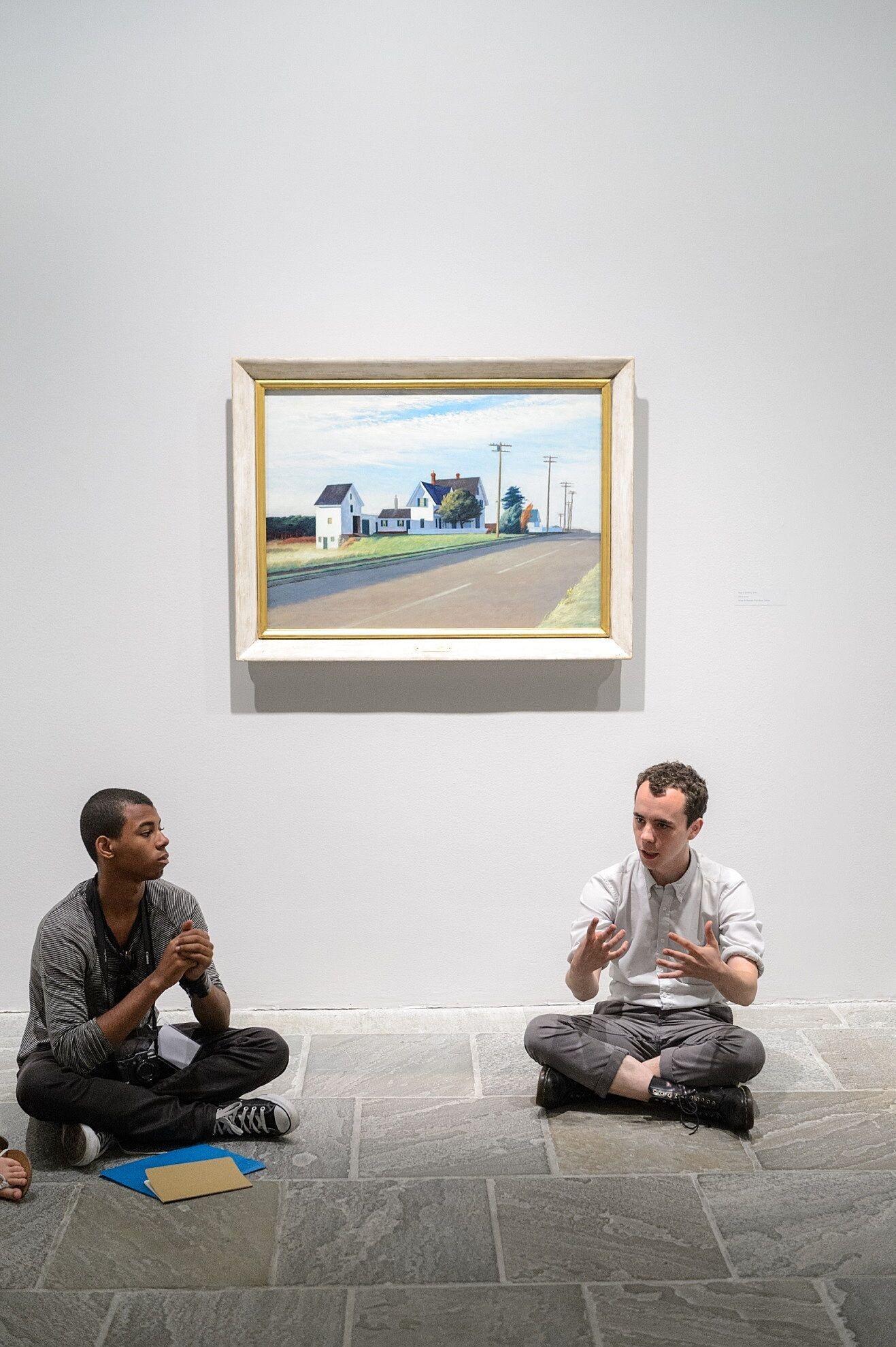 A curator and student sit on the floor in front of an Edward Hopper painting.