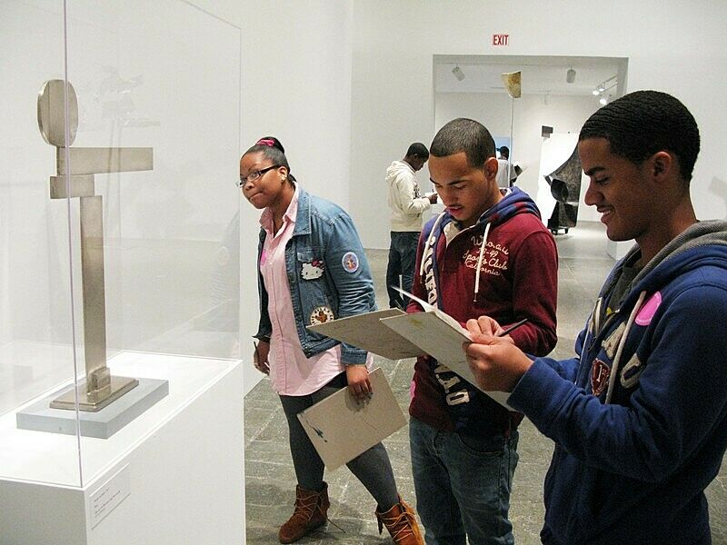 three students with notepads in front of sculpture