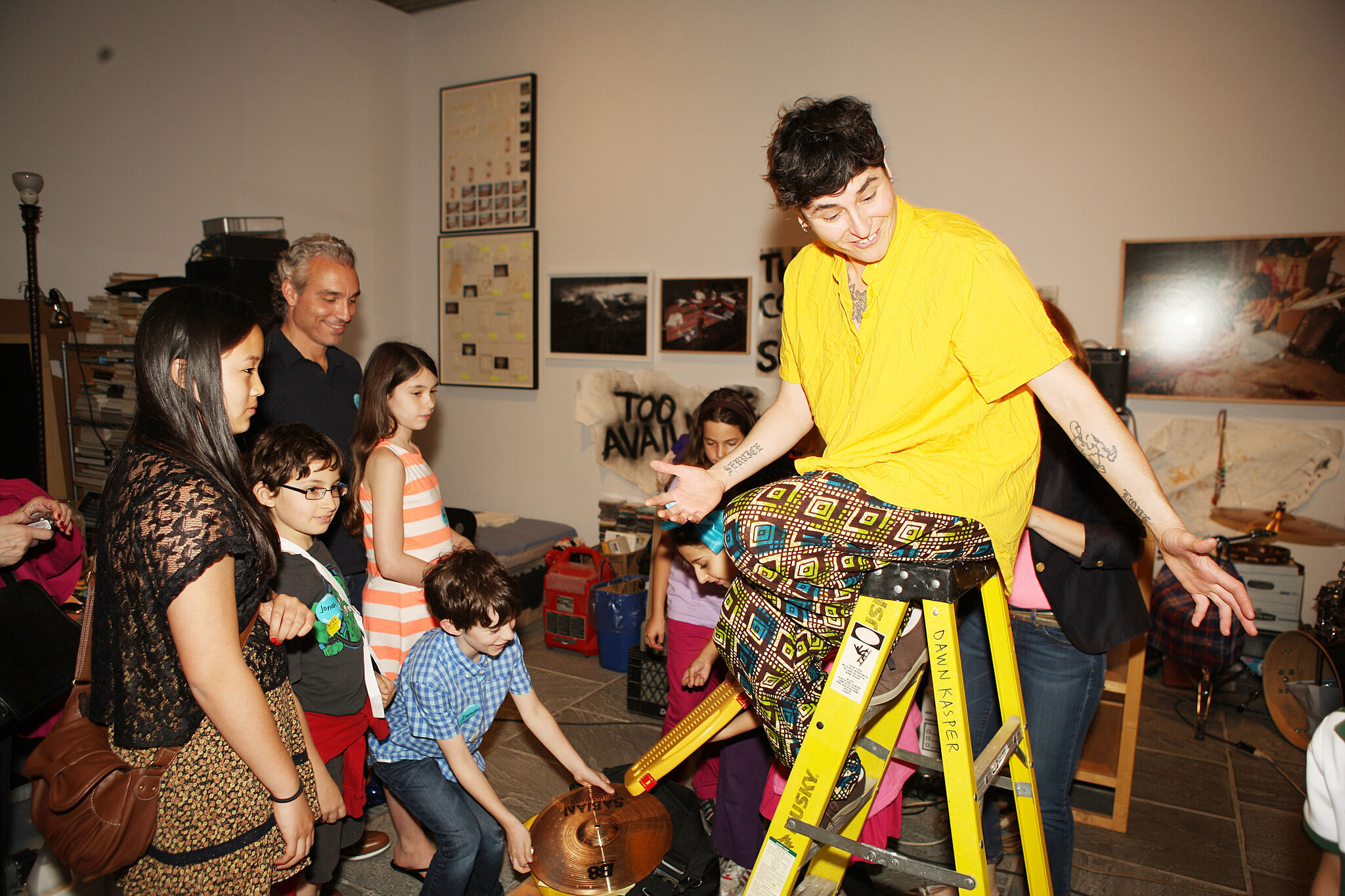 The artist sits on a ladder surrounded by families