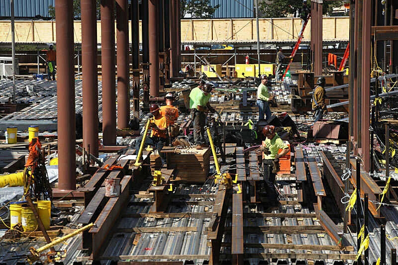 Workers laying down the floor surrounded by beams.