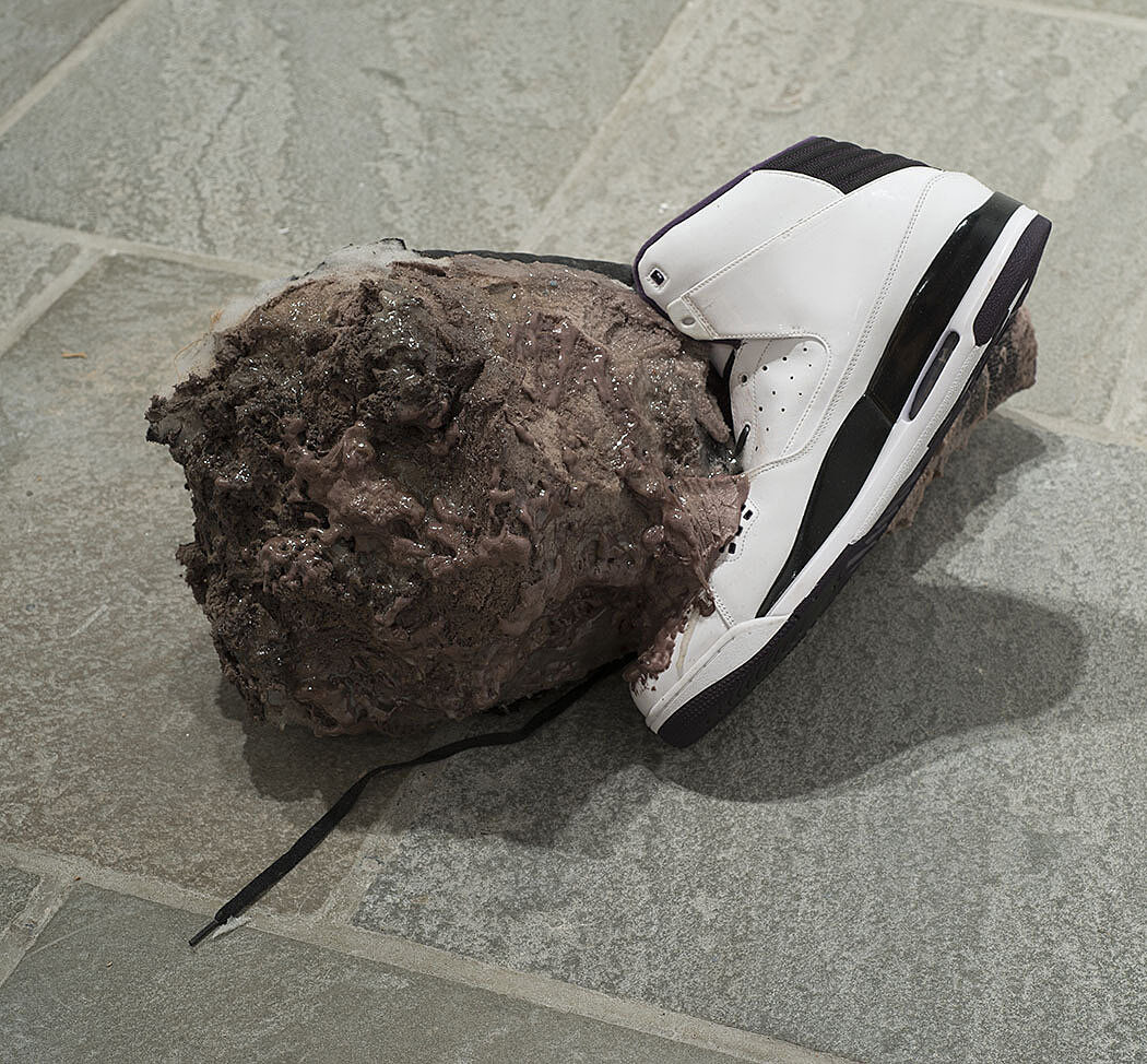 A sculpture of a shoe attached to a brown mass.