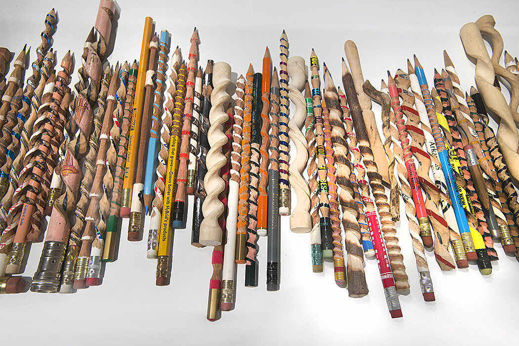 Carved pencils and sticks lined up on a white surface.