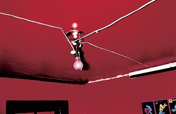 A lightbulb attached to the ceiling of a red room.