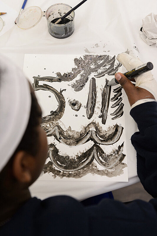 A child making abstract marks on paper with black paint marker