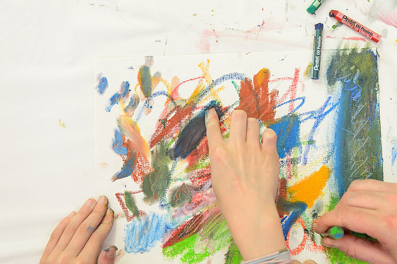 Three hands create a colorful composition with oil pastels