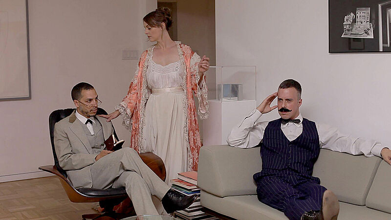 Two men sit in period attire, looking concerned, while a woman comforts the one on the left