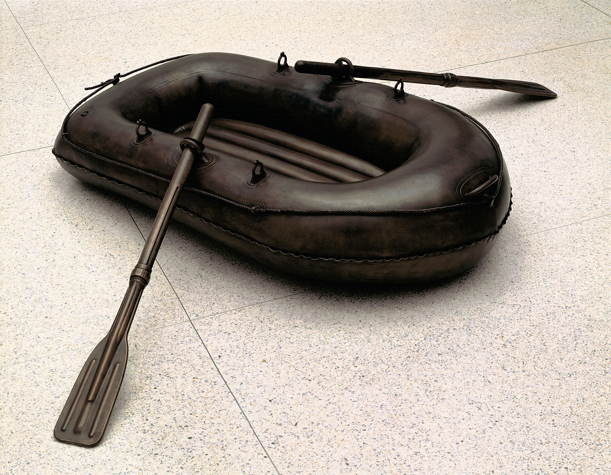 A sculpture of a black lifeboat with two oars on the ground.