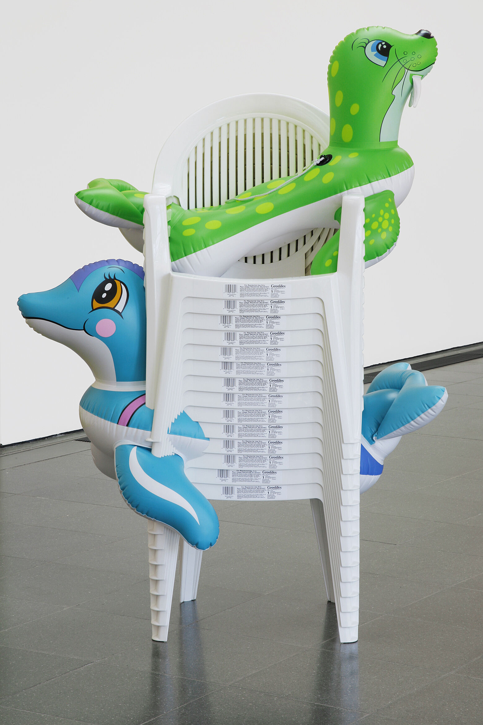 A sculpture of two inflatable seals stuck in a stack of chairs.
