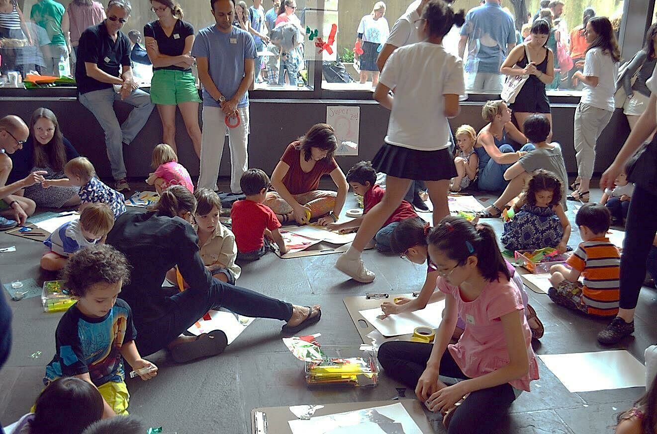 Families sit on the ground and collaborate on art projects. 