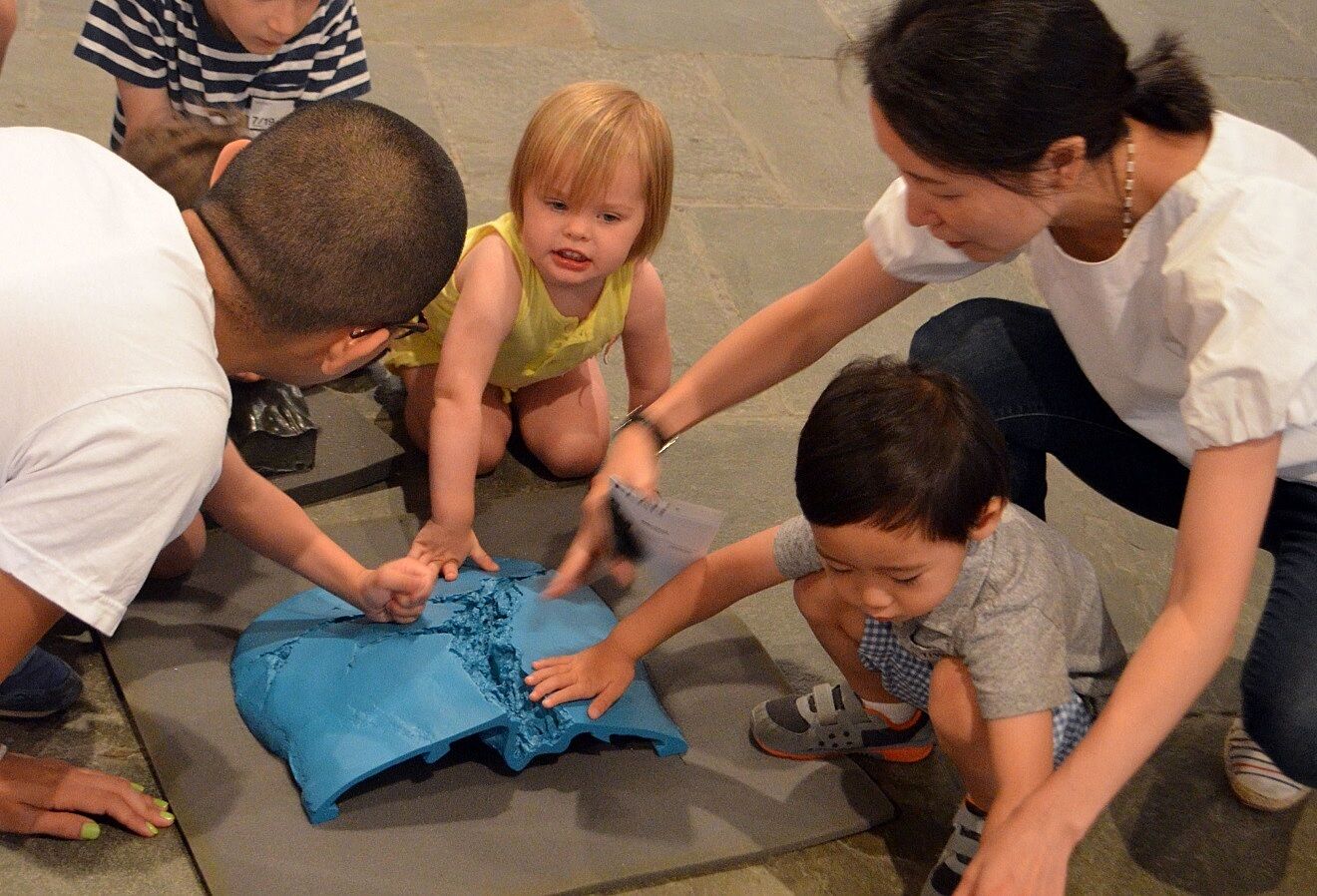 Families interact with a blue sculpture by Jeff Koons.