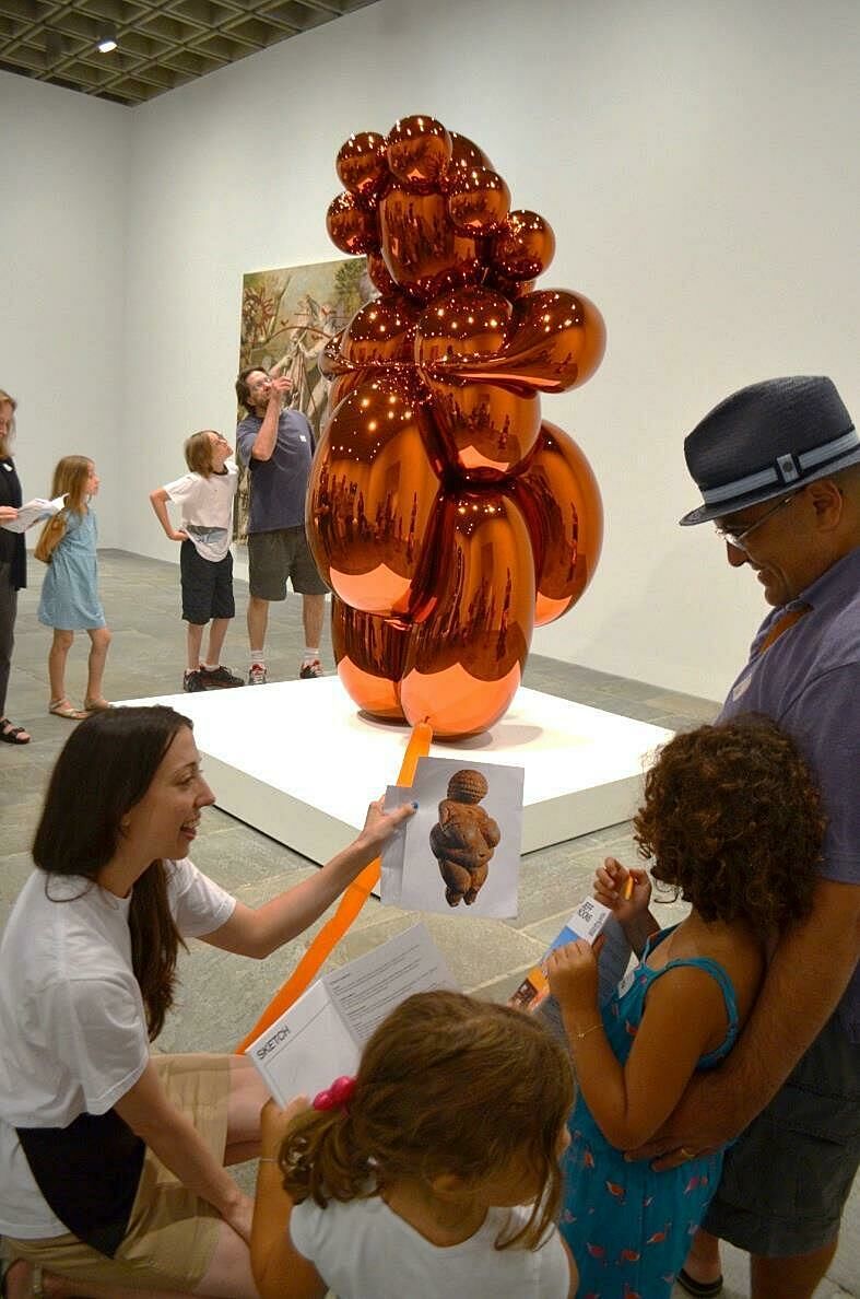 A museum staff member shows a family the inspiration behind a Jeff Koons sculpture.