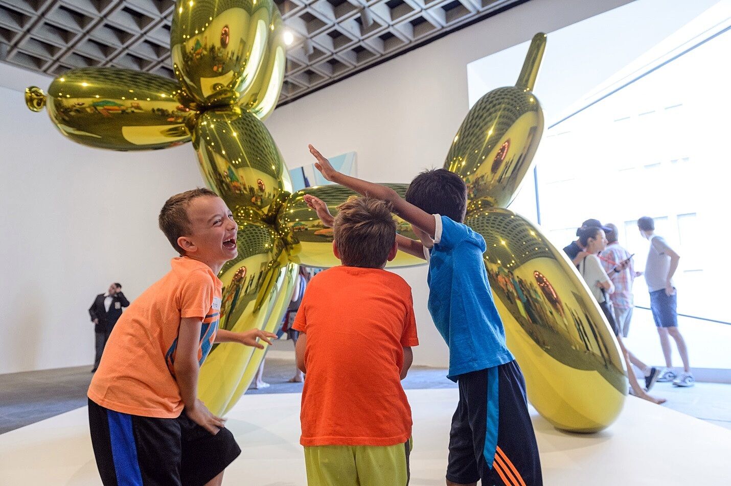 Kids laugh in front of a sculpture of a balloon dog