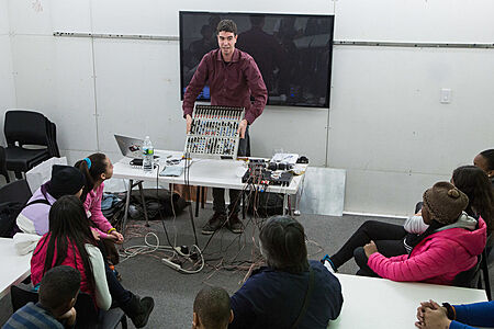 The artist shows students an electronic device with many controls