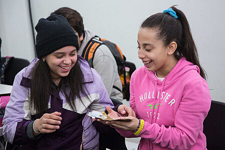 Two students laugh at small device in the palm of one student's hand