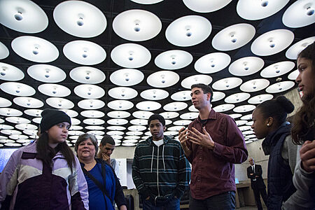 The artist addresses students under bright white circular lights