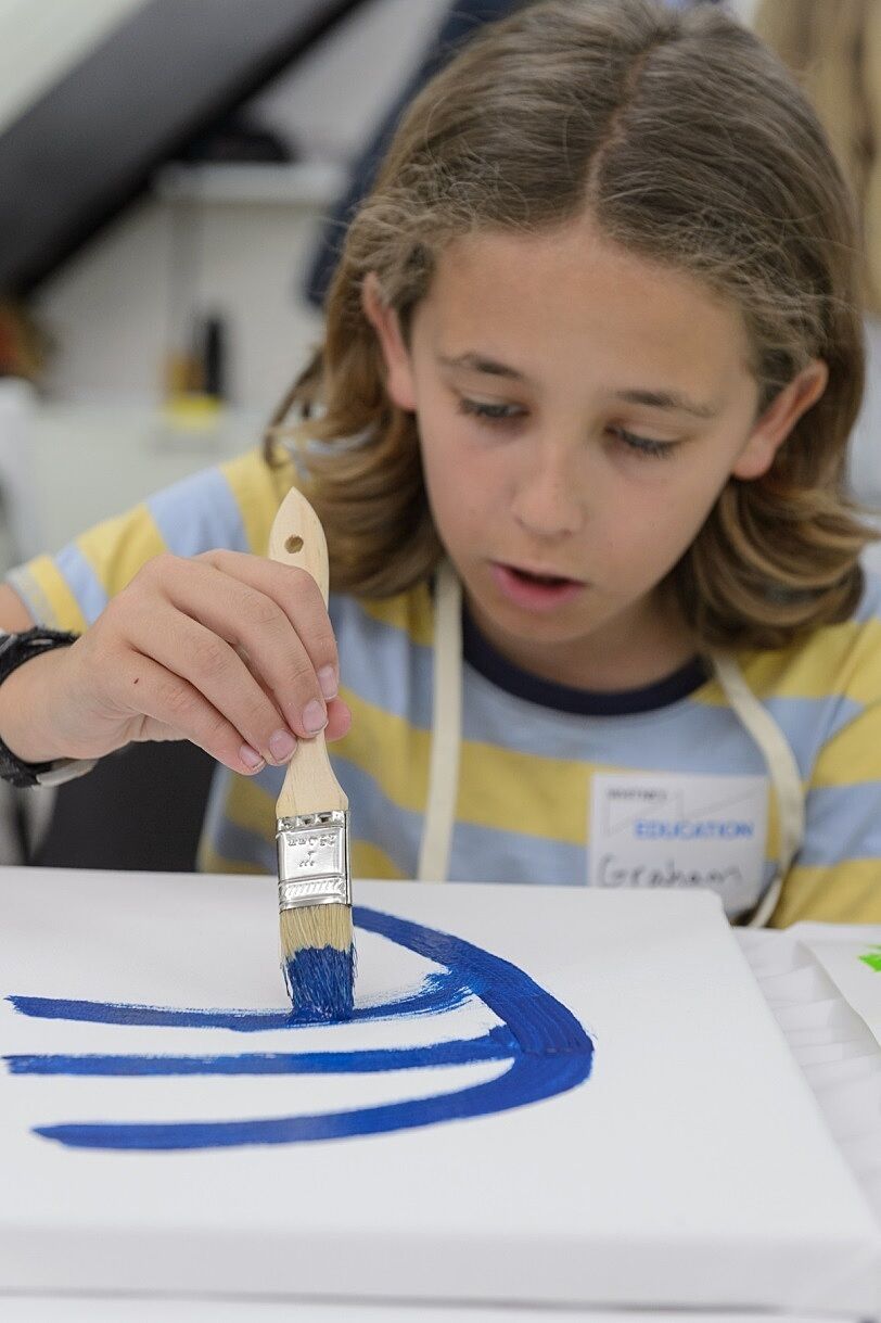A child paints with a rich blue onto a blank canvas.