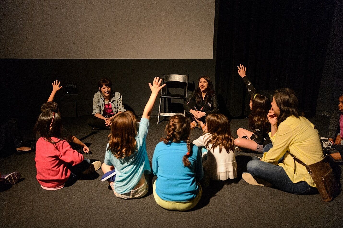 Children and parents raise their hands with questions in a circle around the artist.