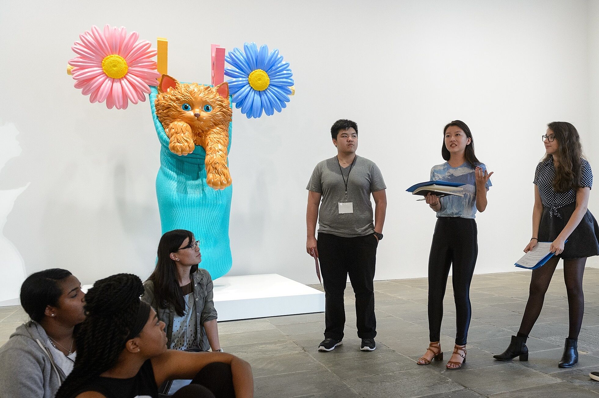 Teens stand talking next to a sculpture of a cat in a bag.