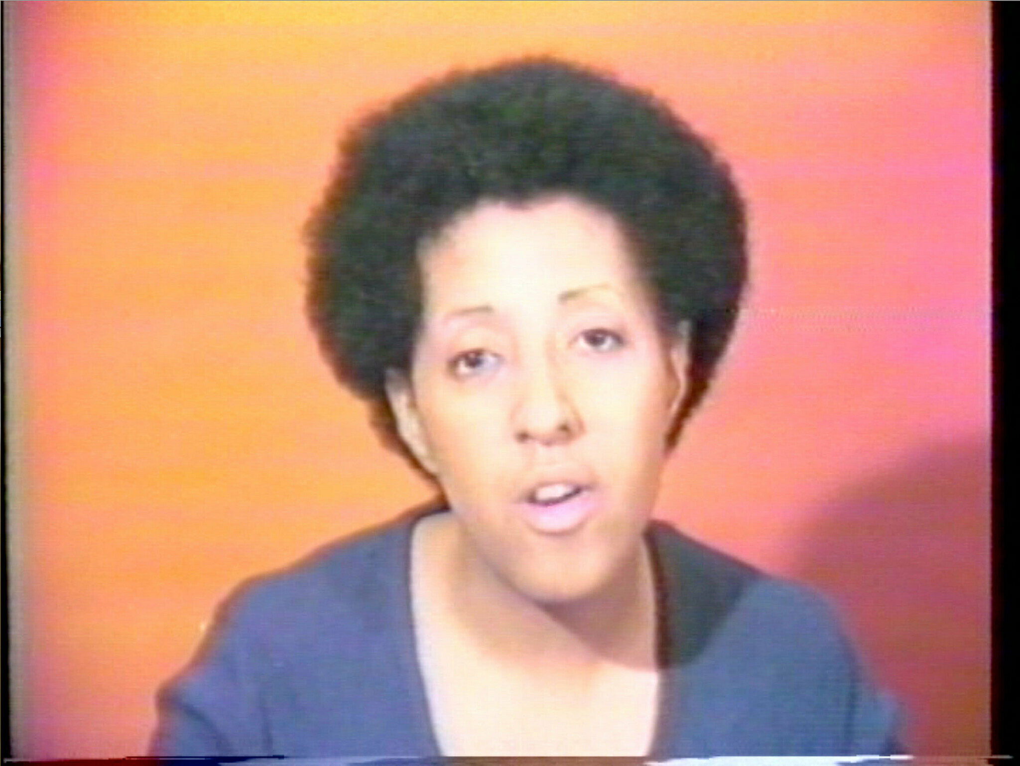 Film still of a woman's head against an orange background.