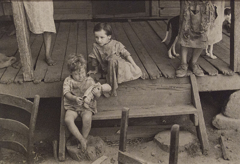 A photograph of children sitting on a stoop with adults and a dog standing behind them.