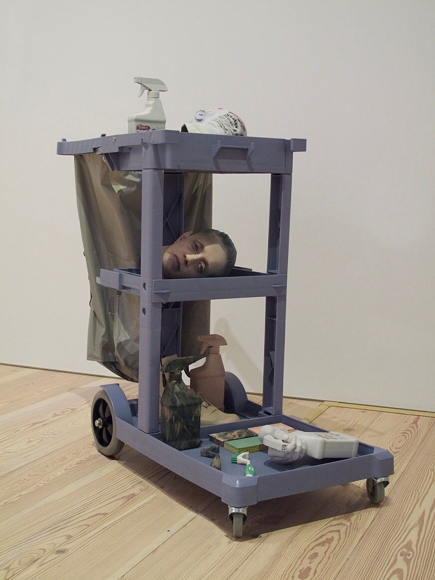 A sculpture of a custodian&#39;s cart, a head lying on the middle shelf.